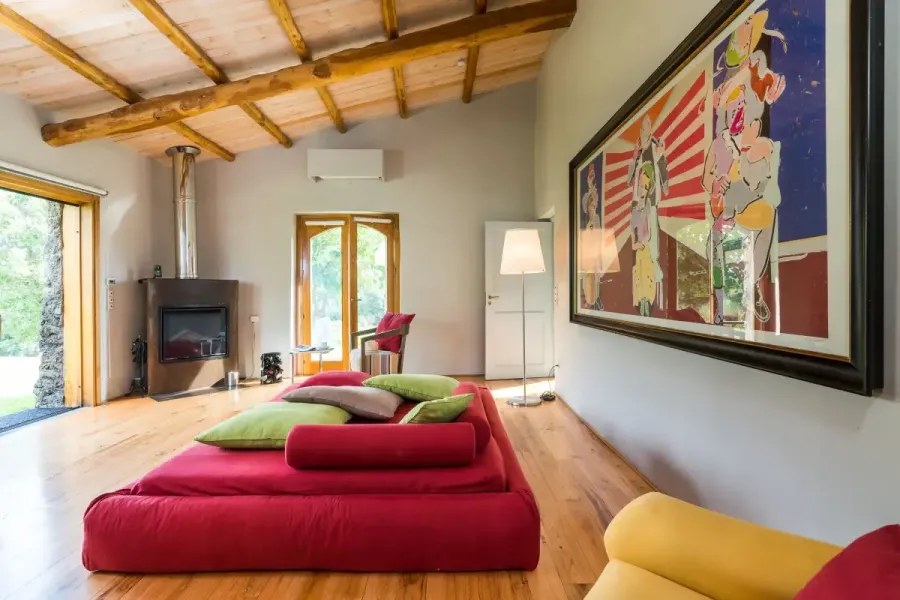 Soggiorno accogliente e colorato, con divano rosso, arte vivace e camino moderno.